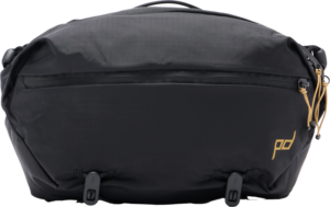 800q-01_129772 Peak Design Outdoor Sling 7L - musta -mallistossa on vetoketju edessä, kultainen logokirjoitus oikeassa alakulmassa, ruskehtavat vetoketjunvetimet oikealla puolella ja kaksi säädettävää hihnaa alareunassa.