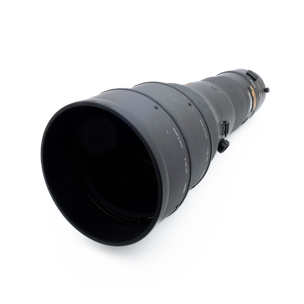 Nikno 400mm f_28G ED VR-4 Nikon AF-S Nikkor 400mm f/2.8G ED VR -objektiivi (käytetty, ALV 25,5 %, 6 kuukauden takuu) näkyy valkoisella pinnalla matalasta kulmasta, jolloin sen musta lieriömäinen muotoilu ja kuvioidut tarkennusrenkaat korostuvat.