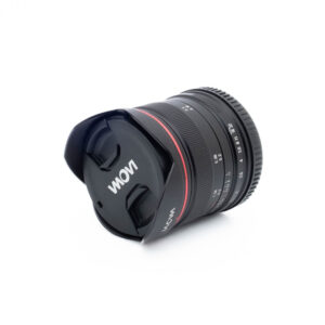 Laowa 7.5mm f/2 C-Dreamer MFT (Kunto K5) - Käytetty objektiivi, jossa on suojus ja suojus kiinnitettynä, makaa kyljellään valkoista taustaa vasten.