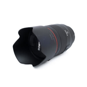 Canon RF 50mm f12 L USM-3 Canon RF 50mm f/1.2 L USM (Takuuta 6kk) - Käytetty -objektiivi, johon on kiinnitetty linssinsuojus, on kuvattu kulmassa valkoisella taustalla. Siinä näkyy punainen rengas ja näkyvä Canon-brändi.