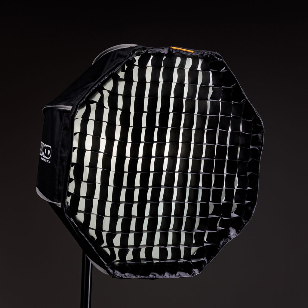 1623067157_424 MagMod Magbox Pro 24 Octa Grid, musta kahdeksankulmainen softbox, jossa on ritilädiffuusori, on asennettu jalustalle tummaa taustaa vasten ammattimaiseen studiovalaistukseen.