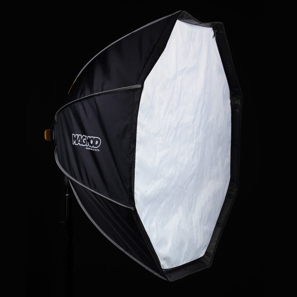 1623067447_947 MagMod MagBox Pro 42 Octa, suuri kahdeksankulmainen softbox, jossa on valkoinen diffuusoripaneeli ja mustat sivut, asennettuna jalustalle mustaa taustaa vasten. MagModin logo on näkyvissä sen kyljessä.