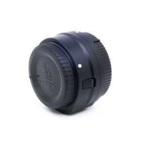 Nikon FTZ II-3 Musta Nikon FTZ II -adapteri (Kunto K5) - Käytetty näkyy kulmassa valkoista taustaa vasten, ja siinä on objektiivin suojus, kuvioidut pintatiedot ja kiinnityspiste.