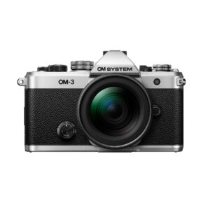 Hopean ja mustan värisen OM System OM-3 + 12-45mm f/4 Pro -kameran etukuva, jossa on suuri objektiivi, yksityiskohtaiset painikkeet, valitsimet ja kuvioitu kahva, eristettynä valkoiselle taustalle.