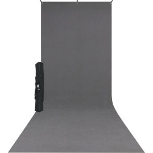 Westcott X Drop Wrinkle Resistant Backdrop Kit, neutraali harmaa (1,5 m x 3,7 m) näkyy ulottuvan seinältä lattialle, ja sen musta kantolaukku, jossa on olkahihna, on sijoitettu taustan vasemmalle puolelle.