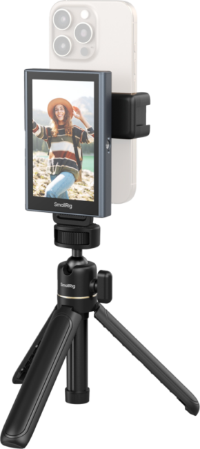 800q-01_132723 Hattupäinen nainen hymyilee ja poseeraa ulkona, kun hänen älypuhelimensa, joka on kiinnitetty SmallRig 4851 Wireless Video Monitor for Phone (Vlog Kit) -laitteeseen, näyttää hänen kuvansa näytöllä.