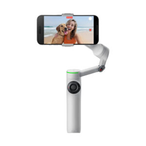 Insta360 Flow 2 Pro Standard _0004_Layer 1 Insta360 Flow 2 Pro Standard Bundle - Stone Grey -gimbaali pitää älypuhelinta, joka tallentaa hymyilevän naisen ja hänen koiransa poseeraavan rannalla, mikä näkyy puhelimen näytöllä.
