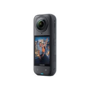 Insta360_X5_0001_1745311568_IMG_2467482 Insta360 X5 Standard Bundle 360-kamera seisoo pystyssä, ja sen näytöllä näkyy kaksi hymyilevää ihmistä ottamassa selfietä auringonlaskun kaupunkimaiseman taustalla.