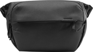 800q-01_123318 Mustassa Peak Design Everyday Sling 10L v2 -rinkassa on moderni läpällinen muotoilu, vetoketjullinen etutasku ja säädettävät hihnat, jotka näkyvät yksiväristä taustaa vasten.