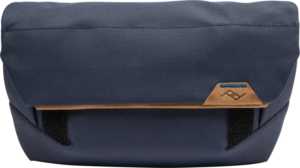 Peak Design The Field Pouch v2 // Midnight on suorakulmainen laivastonsininen pussi, jossa on ruskehtavat nahka-aksentit, mustat hihnat ja pieni ommeltu logo edessä.