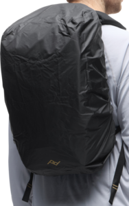800q-01_133347 Vaaleanharmaaseen paitaan pukeutuneella henkilöllä on takaapäin katsottuna musta Peak Design Rain Fly 15L-20L -reppupussi, jonka alaosan lähellä on hienovarainen logo.