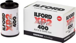 IlfordPhoto Ilford Film XP2 Super 135-36 -filmirulla 35 mm:n filmiä on valkoisen vähittäismyyntipakkauksen vieressä, ja siinä on tuotetiedot ja Harman Technologyn logo.