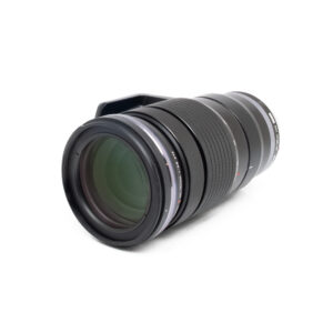 Olympus 40-150mm f/2.8 PRO (Kunto K5, Takuuta 6kk) - Käytetty telezoom-objektiivi, jossa on kuvioitu kahva ja suuri etulasi, näkyy valkoisella taustalla, hieman vasemmalle suunnattuna.
