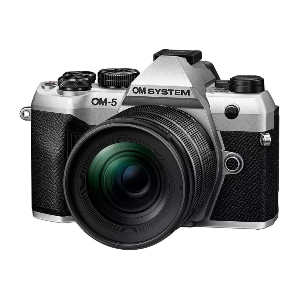 om_system_om-5_mark_ii_hopea_01_12-45mm_02 Hopeinen OM SYSTEM OM-5 Mark II + 12-45mm f/4 Pro -kamera, kuvassa objektiivi kiinnitettynä pienessä kulmassa valkoista taustaa vasten.