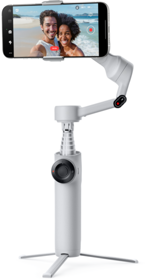 800q-01_133583 The INSTA360 FLOW 2 STANDARD BUNDLE STONE GRAY gimbal with tripod holds a smartphone showing a smiling couple taking selfies on the beach. The stone grey gimbal has an adjustment wheel and extended handle.