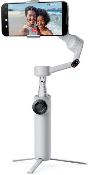 INSTA360 FLOW 2 STANDARD BUNDLE STONE GRAY -kardaani, jossa on kolmijalka, pitää älypuhelinta, jossa näkyy hymyilevä pariskunta ottamassa selfietä rannalla. Kivenharmaassa gimbalissa on säätöpyörä ja pidennetty kahva.
