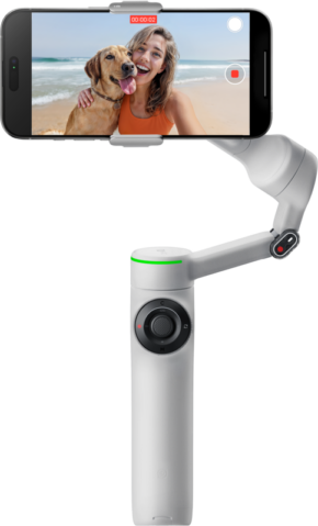 800q-01_133585 INSTA360 FLOW 2 PRO STANDARD BUNDLE STONE GRAY holds a phone showing a selfie video of a smiling woman and a brown dog on the beach. Its control panel has buttons and a green light.