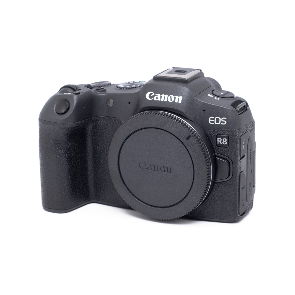 Canon EOS R8-1 Canon EOS R8 (Kunto K5, Shuttercount 1000, Takuu 24kk) - Käytetty näkyy vinossa valkoisella taustalla, ja objektiivin kiinnitys on suojattu suojakorkilla.