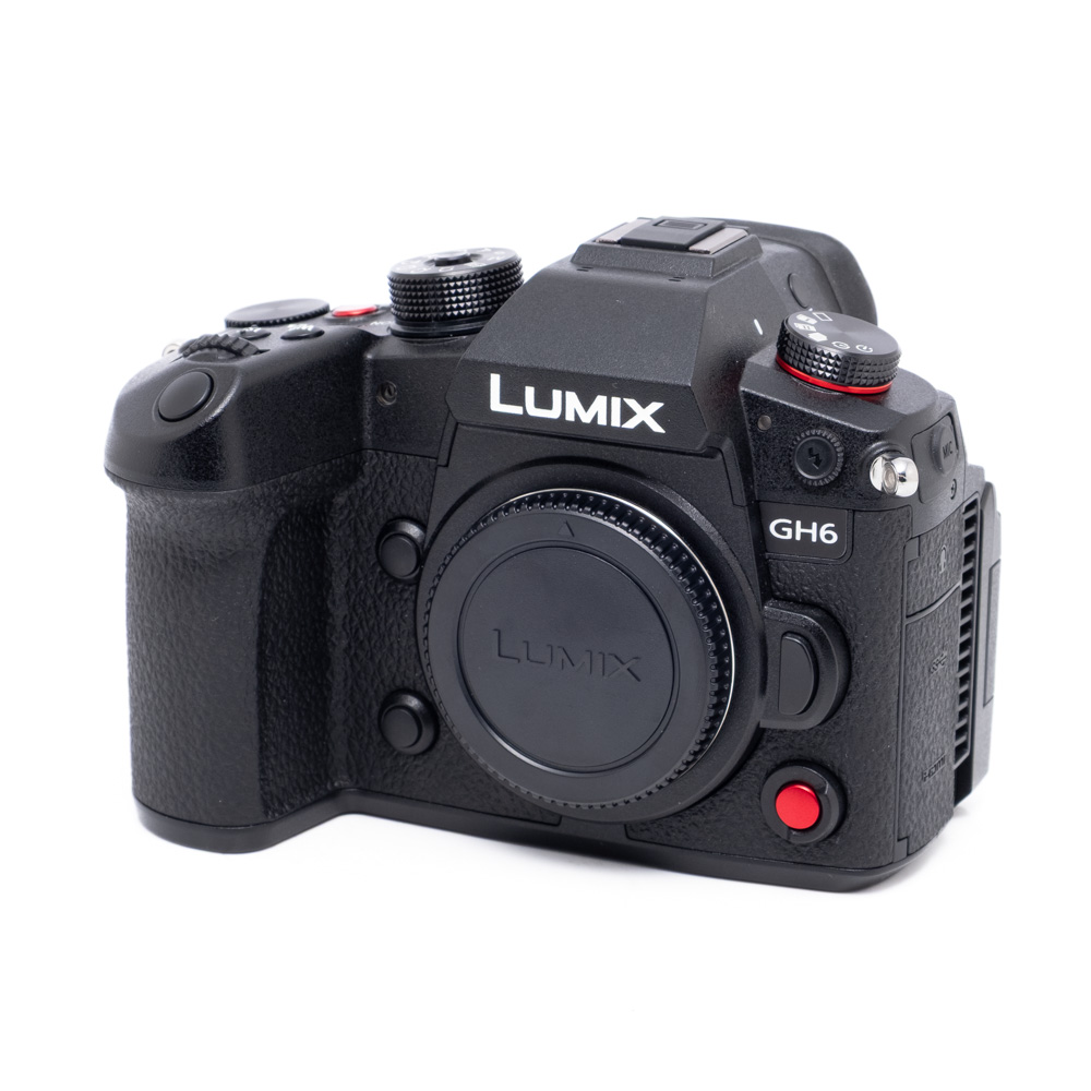 Panasonic Lumix GH6-1 Käytetty Panasonic Lumix GH6 (SC 300, Kunto K5, Takuu 6kk, sis. ALV25,5%) mustan värinen digitaalikameran runko ja objektiivin suojus vinossa valkoisella pohjalla.