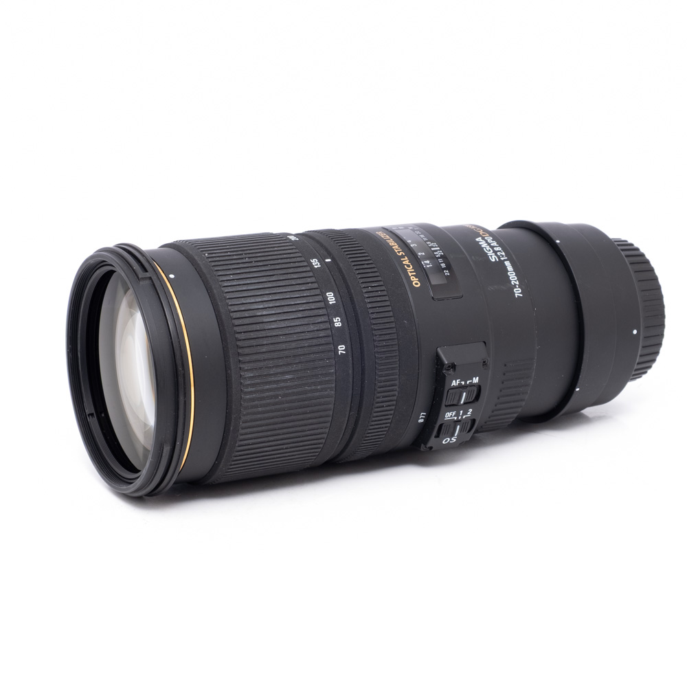 Sigma 70-200mm f2.8 DG HSM Canon-2 Sigma 70-200mm f/2.8 APO OS DG HSM Canon EF -objektiivi, käytetty, musta, jossa on zoomaus- ja tarkennusrenkaat, säätökytkimet ja kultainen rengasyksityiskohta valkoisella pohjalla.