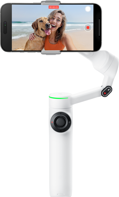 INSTA360 FLOW 2 PRO STANDARD BUNDLE (SUMMIT WHITE) pitää kädessään älypuhelinta, joka kuvaa hymyilevää naista ja hänen koiraansa poseeraamassa hiekkarannalla, ja kohtaus näkyy puhelimen näytöllä.