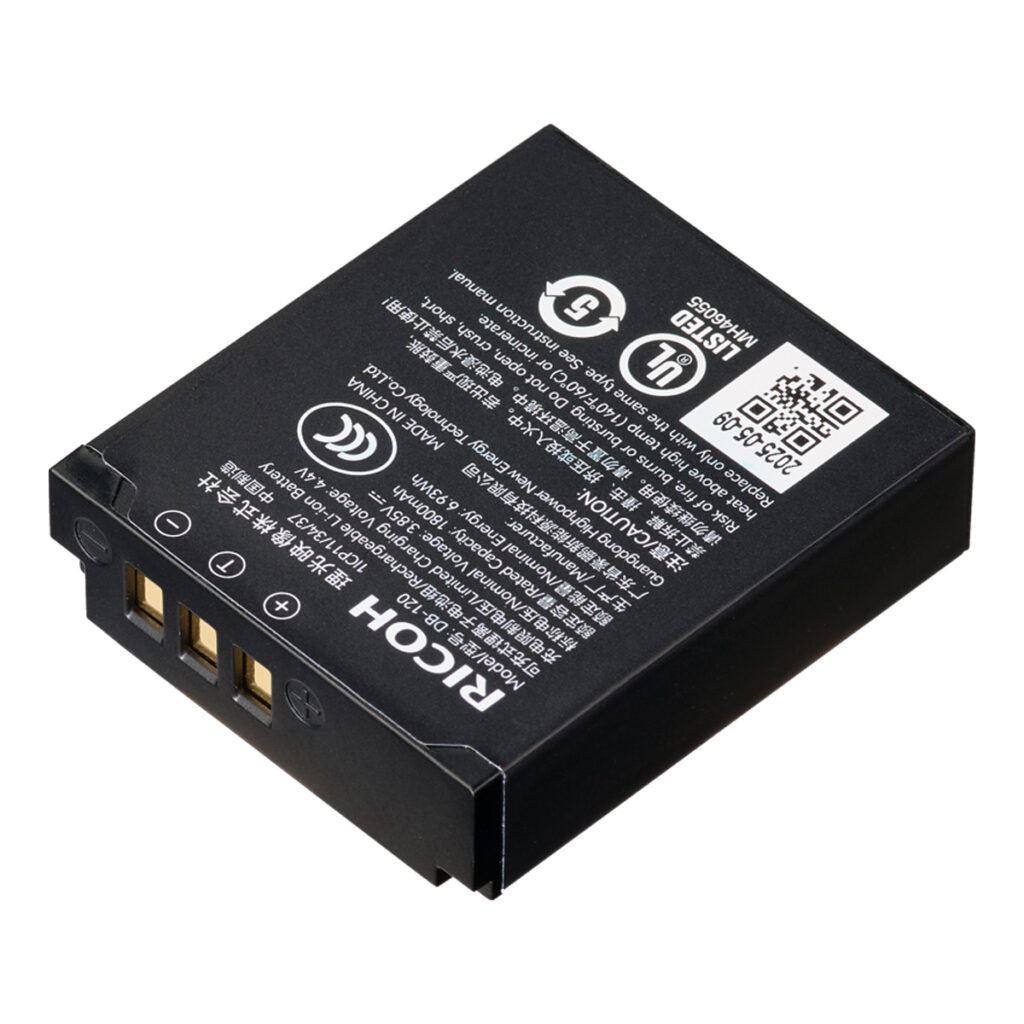 RichAkku Suorakulmainen Ricoh Rechargeable Battery DB-120 -akku, jossa on kullanväriset liitäntänastat, valkoinen teksti, kuvakkeet ja QR-koodi päällä, näkyy vinossa valkoista taustaa vasten.
