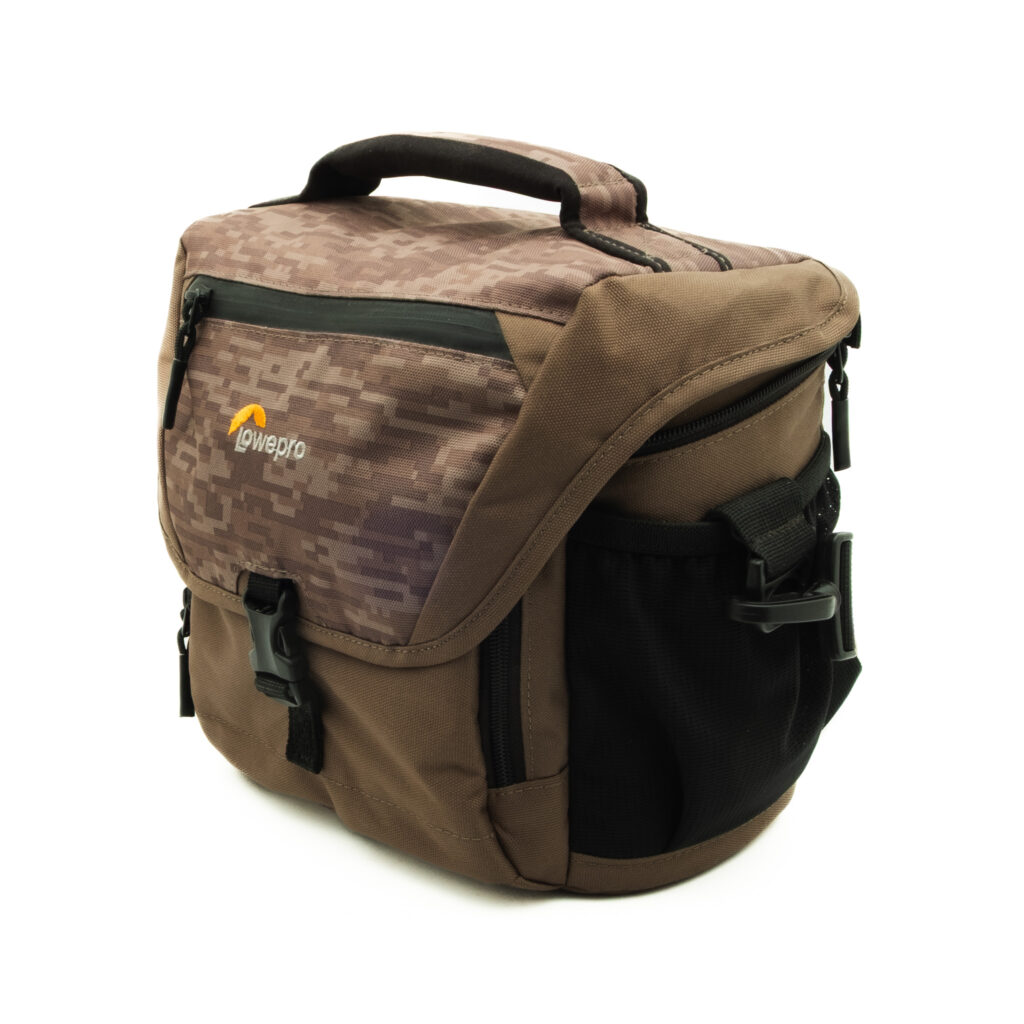 nova170 Lowepro Nova 170 AW II kameralaukku - Käytetty, ruskea, jossa on digitaalinen maastokuvioitu läppä, mustat soljet, verkkomaiset sivutaskut ja pehmustettu yläkahva, kuvassa valkoista taustaa vasten.