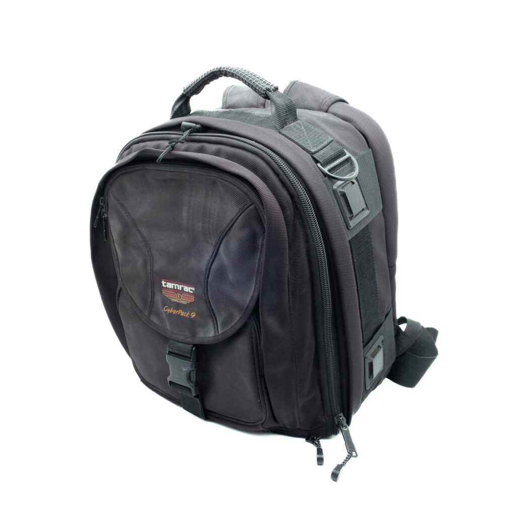 Tamrac Cyberpack 9 Musta Tamrac Cyberpack 9 reppu - Käytetty, jossa on useita vetoketjullisia lokeroita, pehmustetut olkahihnat ja kantokahva ylhäällä, kuvassa valkoista taustaa vasten.