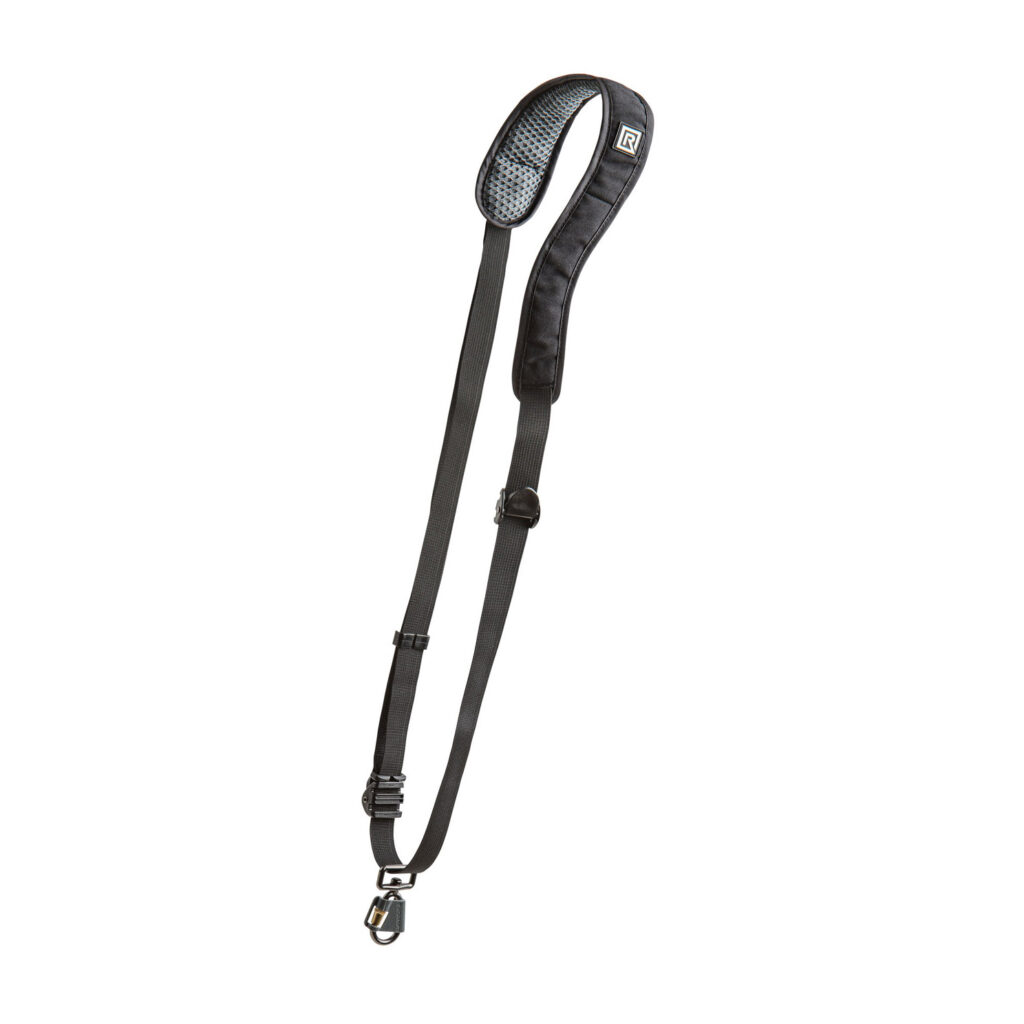 © BryCox.com, Bry Cox BlackRapid RS W2 Camera Sling for Women -kamerahihna on musta säädettävä hihna, jossa on pehmustettu olkaosa ja metalliklipsi, joka näkyy valkoisella pohjalla.