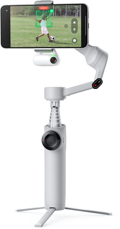 800q-01_133584 Lapsi pelaa jalkapalloa kentällä, kun jalustalla varustettuun Insta360 Flow 2 AI Tracker Bundle Stone Gray -gimbaaliin kiinnitetty älypuhelin tallentaa ja näyttää toiminnan reaaliajassa.