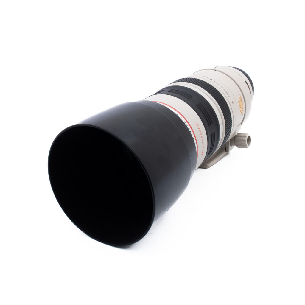 Canon 100-400mm f45-56 L IS USM-3-4 Valkoisella pohjalla on suuri valkoinen telekameran objektiivi, jossa on musta vastavalosuoja ja jossa on punaisia ja kultaisia yksityiskohtia.