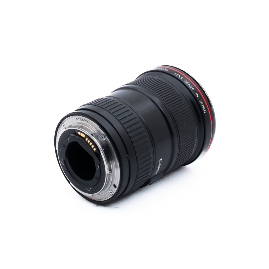 Canon 16-35mm f28 L USM-1 Canon-kameran objektiivi kyljellään, jossa näkyy metallinen kiinnitysrengas ja elektroniset koskettimet. Objektiivi on musta, ja sen etupuolella on punainen rengas ja valkoinen teksti, jossa on sen tekniset tiedot. Tausta on valkoinen.