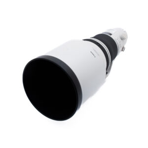 Canon 400mm f28 L IS II USM-3 Suuri valkoinen telekameran objektiivi, jossa on musta etureuna, valkoista taustaa vasten kuvattuna kulmassa, jossa näkyy leveä etupaneeli ja osa piipusta.