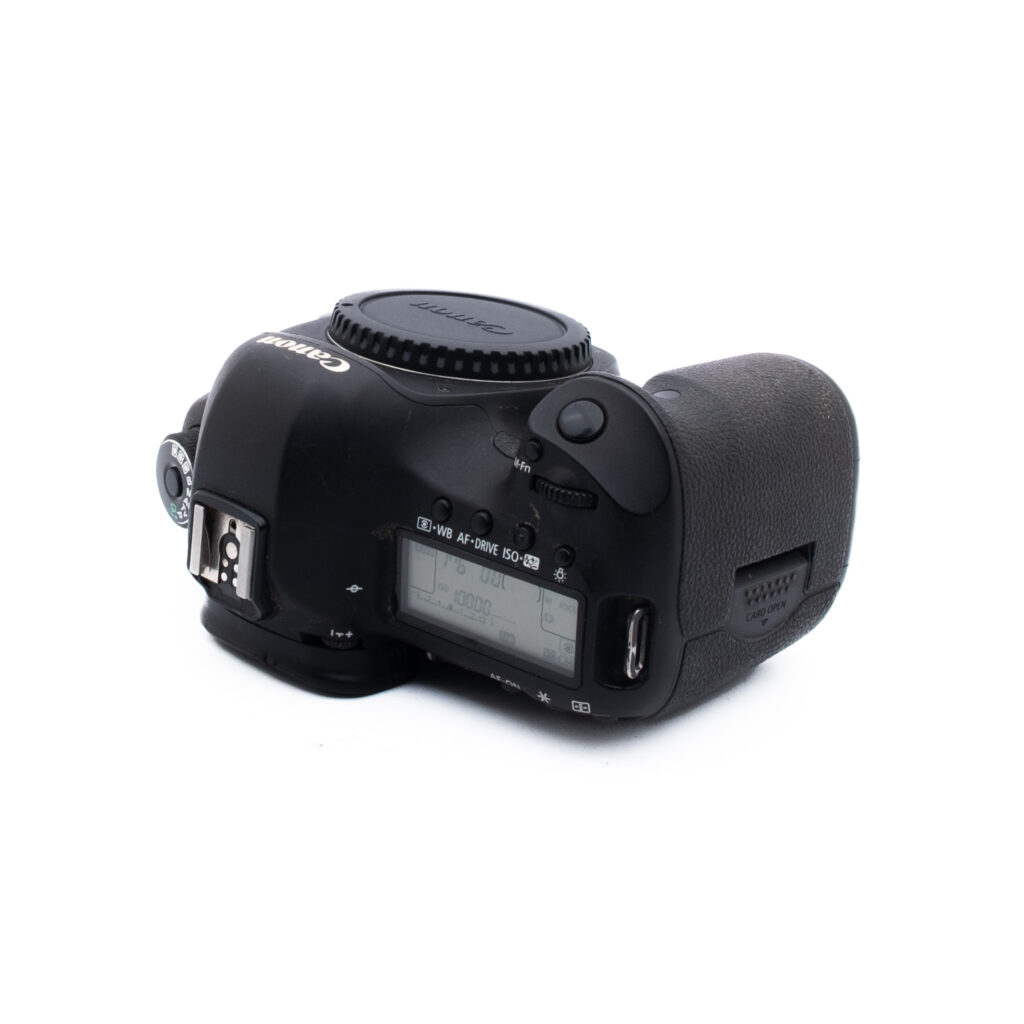 Canon 5D Mark III-2 Mustan Canon DSLR-kameran runko on kuvattu ylhäältä päin, ja siinä näkyvät ohjauspainikkeet, LCD-näyttö ja kuvioitu kahva. Objektiivia ei ole kiinnitetty. Tausta on valkoinen.