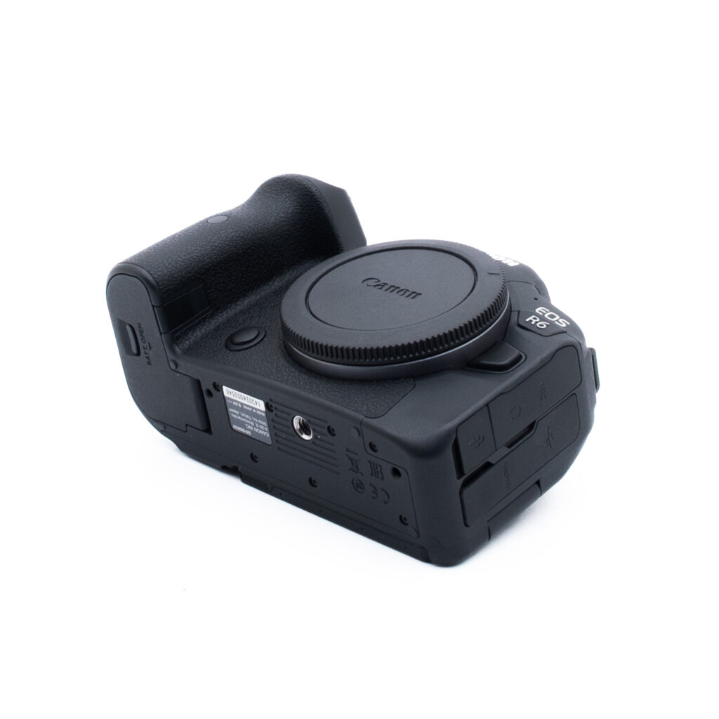Canon R6 3546-1 Valkoisella taustalla näkyy mustan värinen Canon-digitaalikameran runko, josta on poistettu objektiivi ja objektiivin kiinnityksen peittävä suojus. Kamera on sijoitettu vinoon, jolloin sen pohja ja kylki näkyvät.