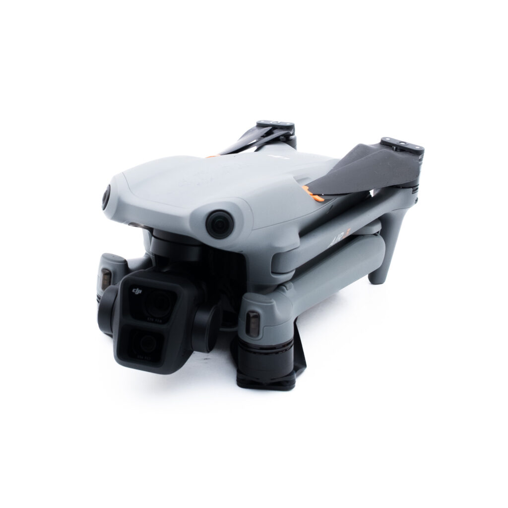 DJI Air 3-6 Pienikokoinen, kokoontaitettu harmaa lennokki, jossa on mustat potkurit ja etukamera valkoisella pohjalla.
