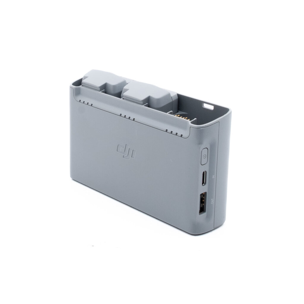 DJI Mini 2 SE-1 Harmaa DJI:n akkujen latauskeskitin, johon on asetettu kaksi akkua ja jonka sivulla on USB- ja USB-C-portit valkoista taustaa vasten.