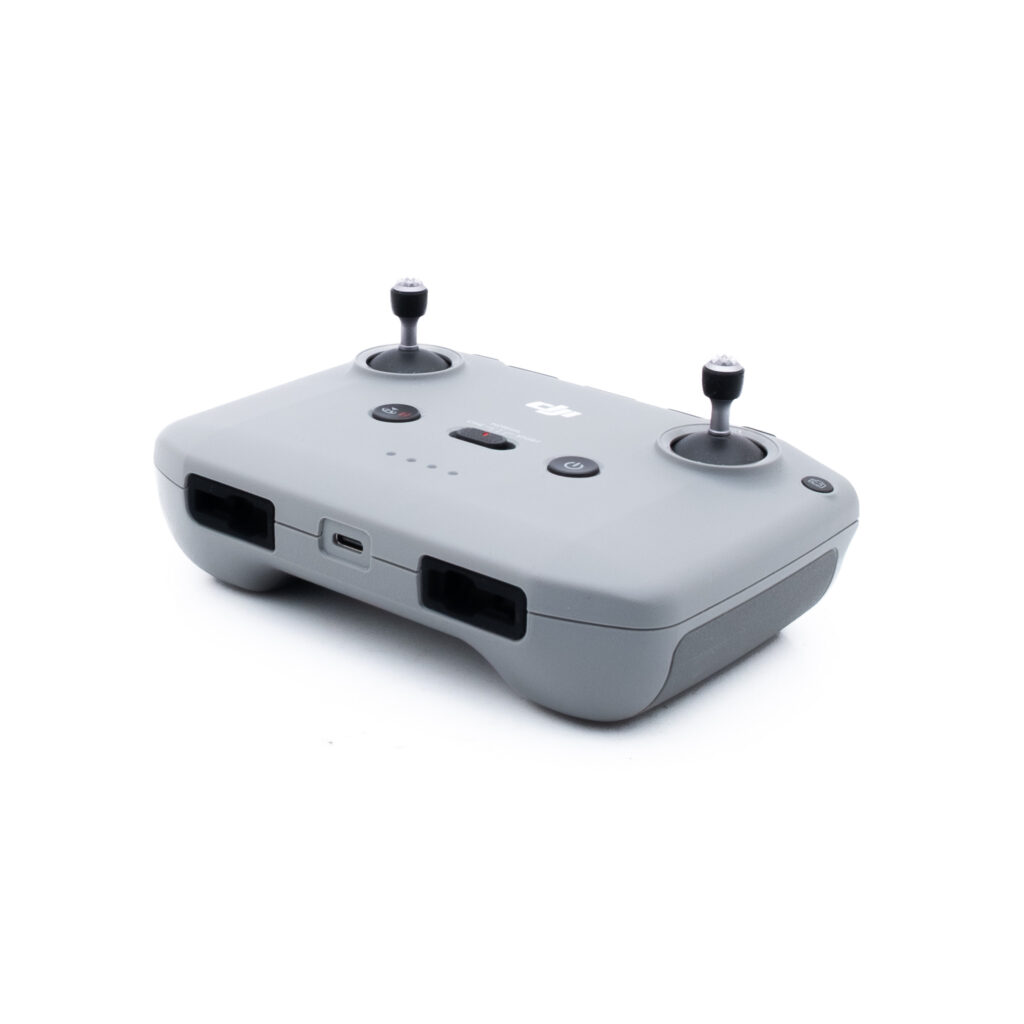 DJI Mini 2 SE-2 Harmaa DJI:n lennokin kauko-ohjain, jossa on kaksi ohjaussauvaa, useita painikkeita ja USB-C-latausportti, kuvattuna valkoisella taustalla.