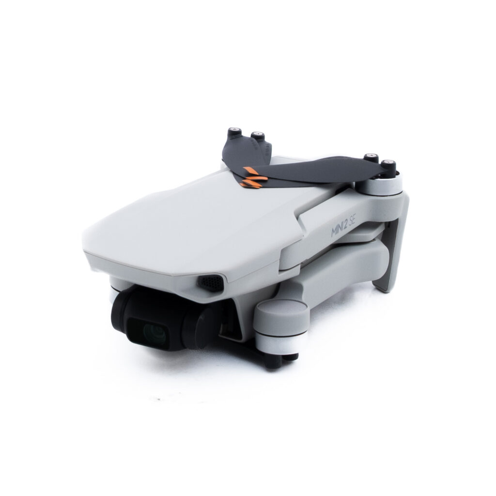 DJI Mini 2 SE-4 Pienikokoinen, kokoontaitettu valkoinen lennokki, jossa on musta kamera ja potkurit, kuvattuna valkoisella taustalla.