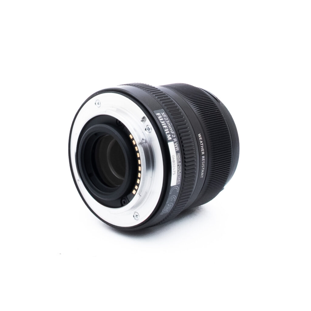 Fuji 23mm f2 R WR-1-2 Musta kameran linssi kyljellään, jossa näkyy metallikiinnitys ja elektroniset koskettimet valkoista taustaa vasten.