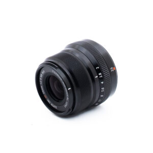 Fuji 23mm f2 R WR-2-2 Musta Fujinon-kameran objektiivi, jossa on valkoisia ja punaisia merkintöjä ja joka on sijoitettu vinoon valkoiselle taustalle. Aukko- ja tarkennusrenkaat sekä objektiivin tekniset tiedot ovat näkyvissä.