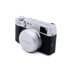 Fuji X100VI-5-3 Hopeanmusta Fujifilm-digitaalikamera, jossa on objektiivin suojus, kuvattuna kolmen neljäsosan kulmassa valkoista taustaa vasten.