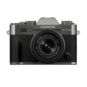 FujiX-T30IIIHarmaaLinssi1 Etukuva harmaasta Fujifilm X-T30 III -kamerasta, jossa on musta kuvioitu kahva ja kiinnitetty XC 13-33mm f/3.5-6.3 OIS -objektiivi, jossa on ylävalitsimet ja Fujifilmin tuotemerkki objektiivin yläpuolella.