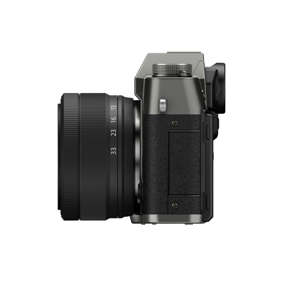 FujiX-T30IIIHarmaaLinssi3 Fujifilm X-T30 III + XC 13-33mm f/3.5-6.3 OIS (harmaa) näytetään sivulta, ja siinä on suuri objektiivi, kompakti kuvioitu runko sekä useita painikkeita ja valitsimia, kaikki valkoista taustaa vasten.