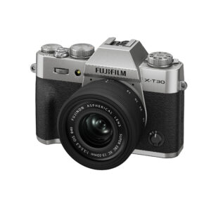 FujiX-T30IIIHopealinssi1 Hopeinen Fujifilm X-T30 III, jossa on XC 13-33mm f/3.5-6.3 OIS -objektiivi, on kuvattu niin, että kameran rungon ja objektiivin etu- ja vasen puoli on näkyvissä.