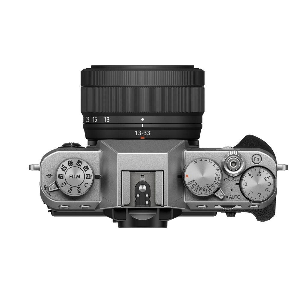 FujiX-T30IIIHopealinssi3 Fujifilm X-T30 III (hopea) -digitaalikameran yläkuva mustalla XC 13-33mm f/3.5-6.3 OIS -objektiivilla, jossa näkyy selkeät hallintalaitteet, toimintatilan ja suljinnopeuden valitsimet sekä oikealla puolella oleva kuvioitu kahva.