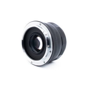 Meike 35mm f14 Nikon Z-1 Lähikuva valkoiselle pinnalle asetetusta kameran objektiivista, jossa metallinen kiinnitys ja lasielementit ovat katsojaan päin, ja objektiivin tynnyri ulottuu taaksepäin.
