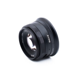 Meike 35mm f14 Nikon Z-2 Musta Meike-kameran objektiivi, jossa on näkyviä lasielementtejä ja kaiverrettuja merkintöjä, on kuvattu kulmassa valkoisella pohjalla.