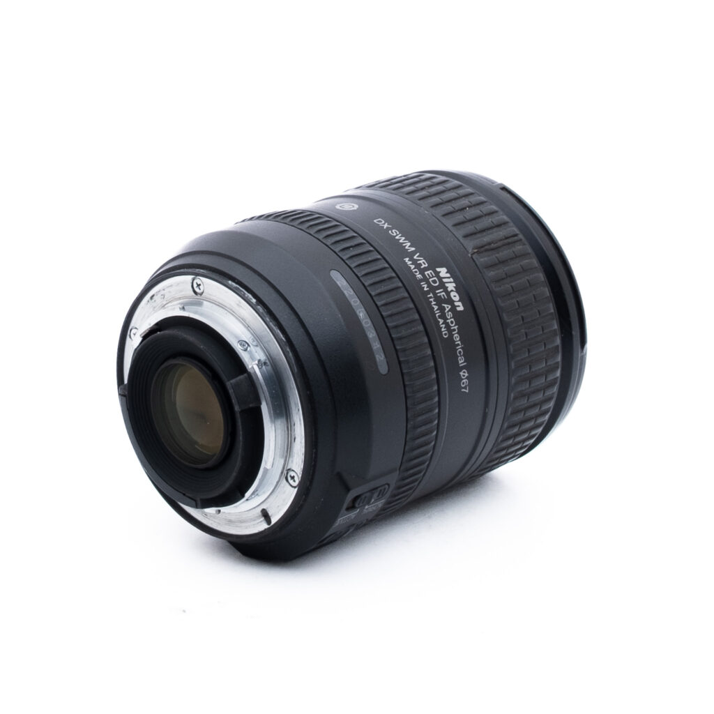 Nikon 16-85mm f35-56G ED DX VR-1 Nikon DX SWM VR 18-55mm -kameran objektiivi näkyy valkoisella pohjalla, ja se on asetettu kulmaan niin, että metallinen kiinnitys ja objektiivin yksityiskohdat näkyvät.