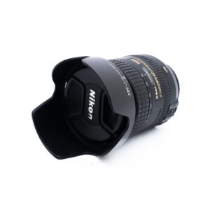 Nikon 16-85mm f35-56G ED DX VR-3 Nikon-kameran objektiivi, johon on kiinnitetty vastavalosuoja, kyljellään valkoista taustaa vasten. Objektiivissa on näkyvät tarkennusrengas ja zoomausrengas, ja siinä on kultaisella ja valkoisella tekstillä merkityt tekniset tiedot.